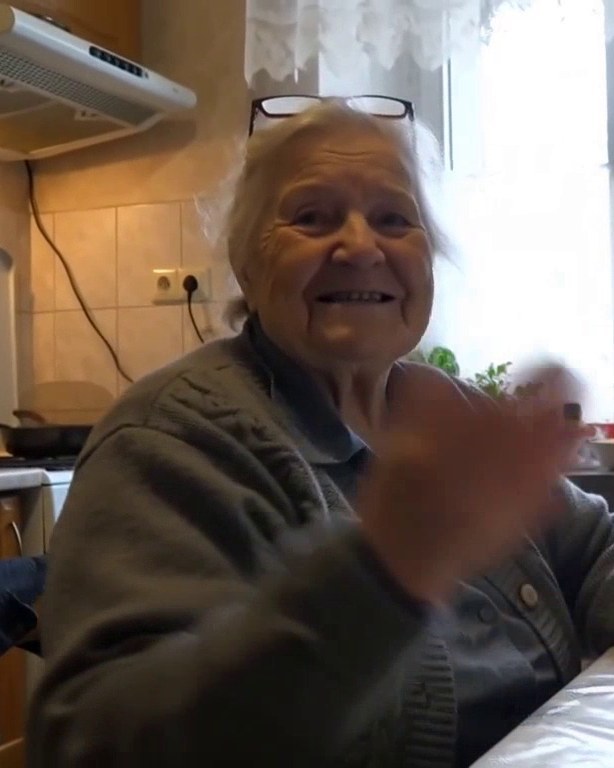 Nagymama a konyhaasztalnál nevetve integet a tabletnek, amelyen a családja üzeneteit nézi